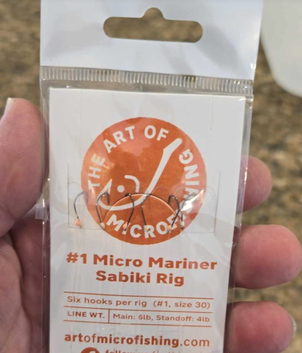 A packet of The Micro Mariner micro fishing sabiki rig, featuring six tiny hooks, alternating colored beads, and durable monofilament lines, neatly packaged on a cardboard line holder with a swivel and snap